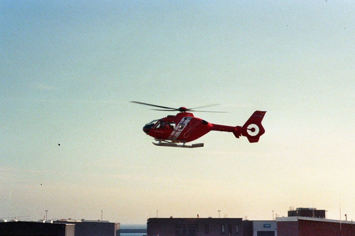 Film photograph: a red rescue helicopter hovering above rooftops in the pale light before sunset