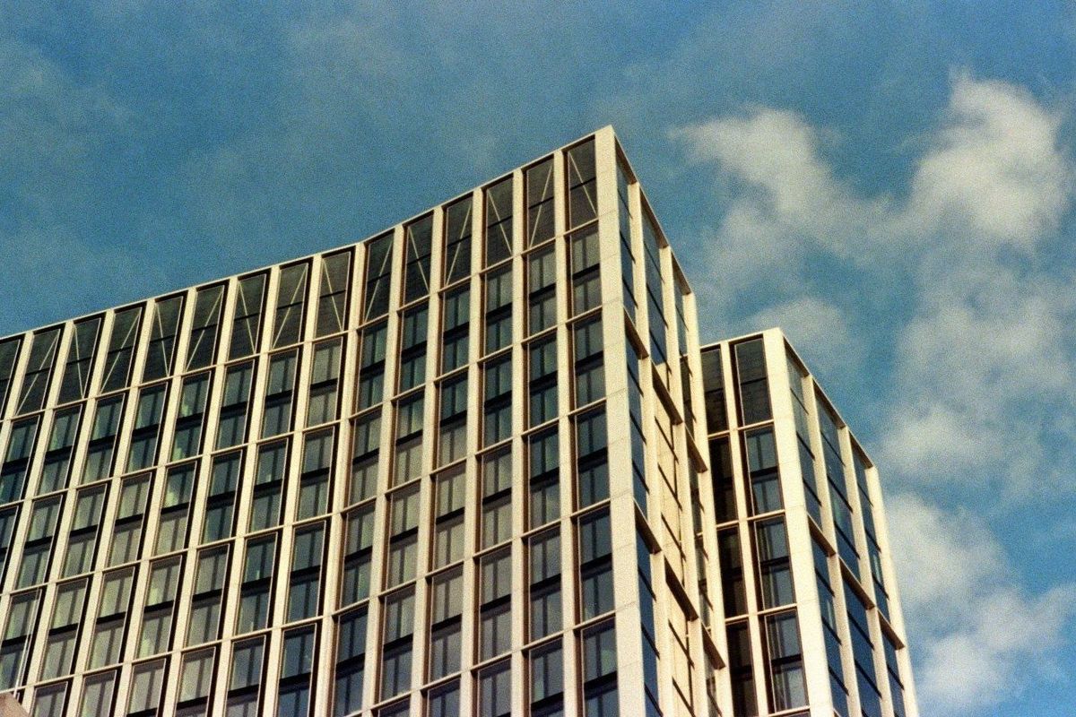 Film photograph: the upper corner of a modern high-rise, its glass facade catching low sun against a blue sky