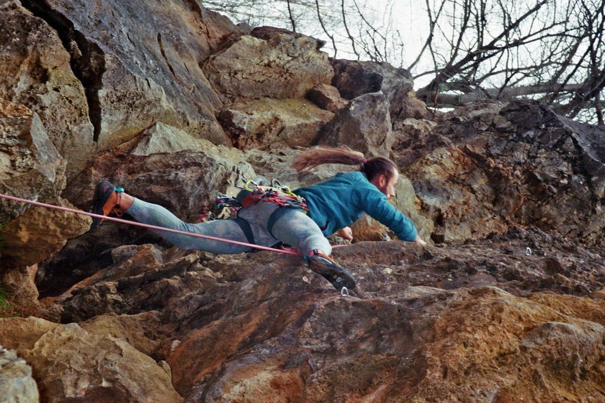 Film photograph: a climber stretched across an overhanging limestone face, rope running below