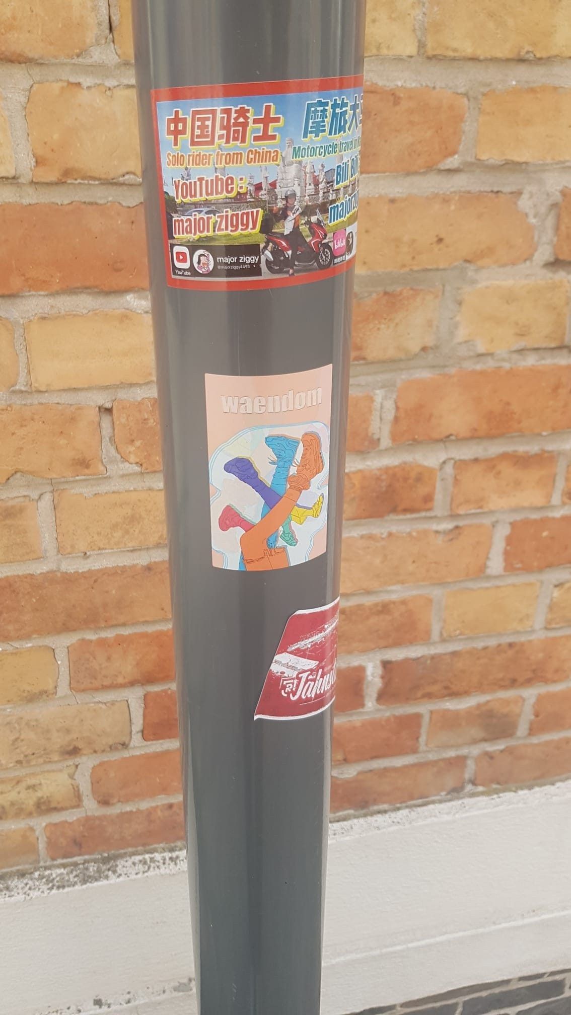 A waendom sticker on a grey pole in front of a brick wall