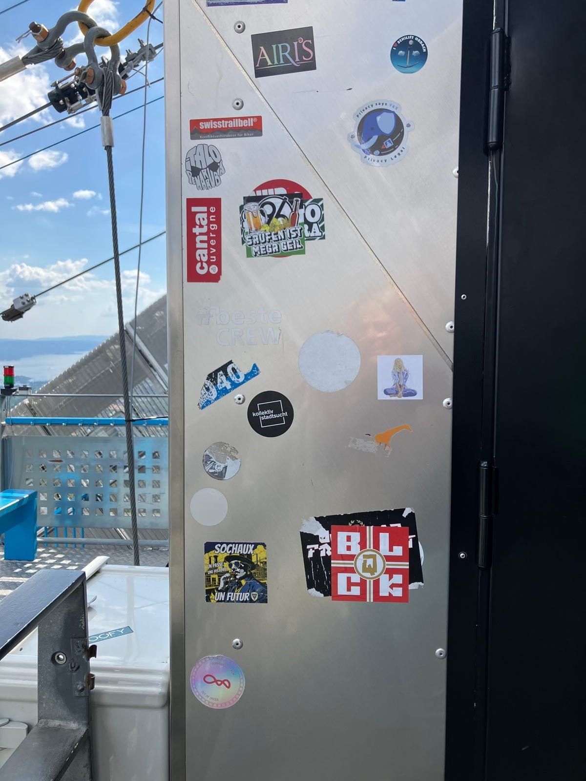 A waendom sticker on the frame of a mountain lift, a lake and hills in the distance