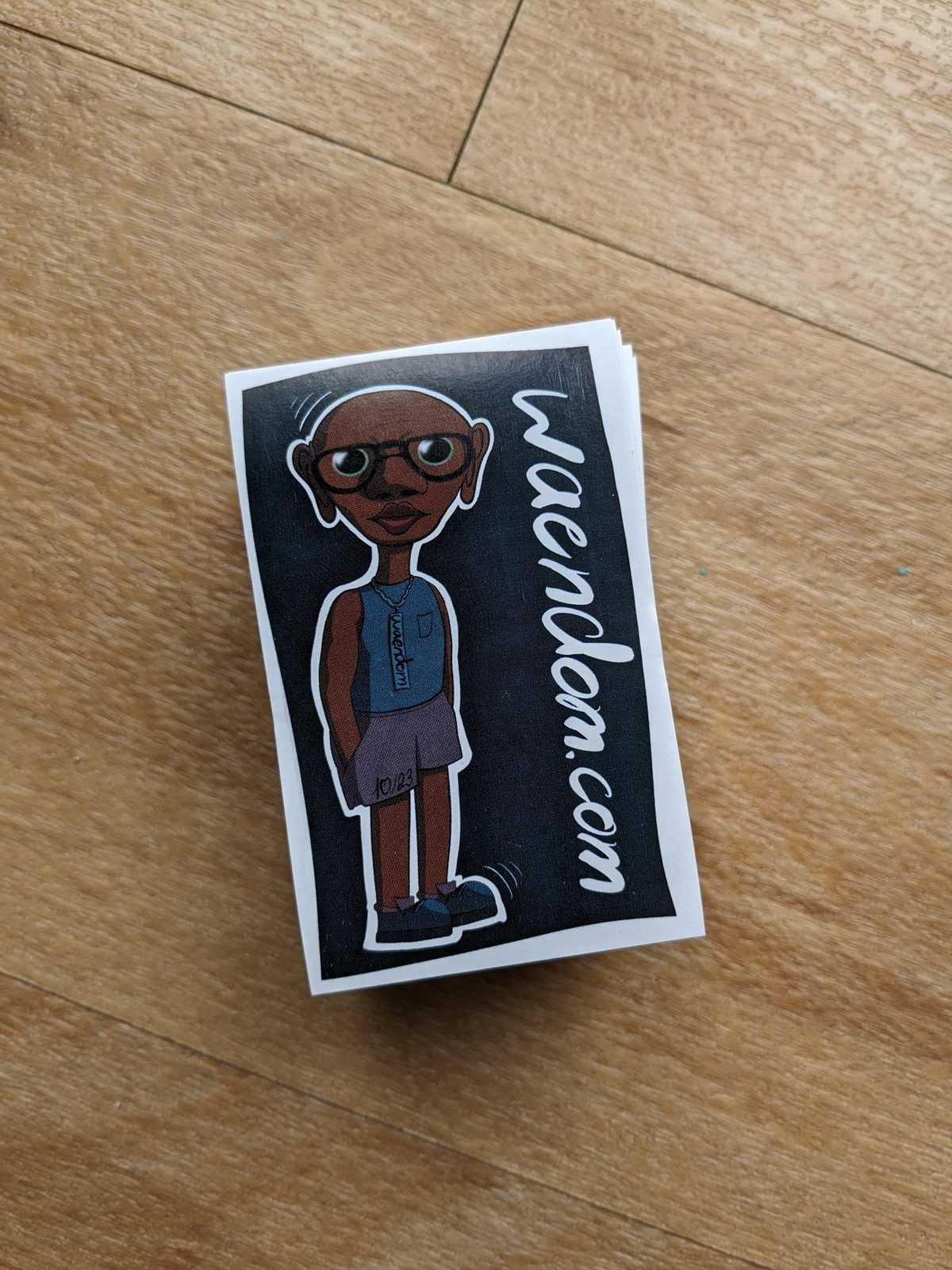 A stack of freshly printed waendom.com stickers on a wooden floor